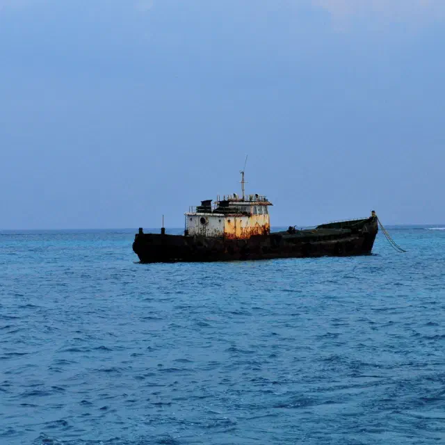 Rusty abandoned boat floating alone on calm blue ocean water under a clear sky.