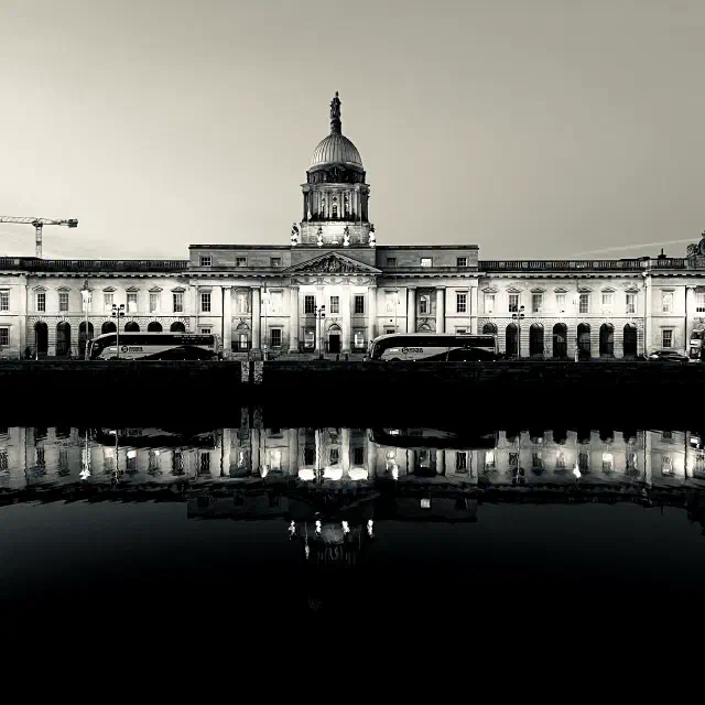 Black-and-white photo of The Custom House in Dublin lit at dusk, reflected in the dark water of the River Liffey.